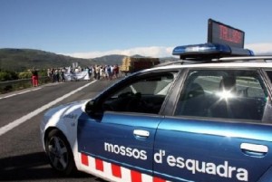 Un cotxe dels Mossos d'Esquadra en primer pla, amb els pagesos que han tallat la C-14 a Alcover al darrere Un cotxe dels Mossos d'Esquadra en primer pla, amb els pagesos que han tallat la C-14 a Alcover al darrere